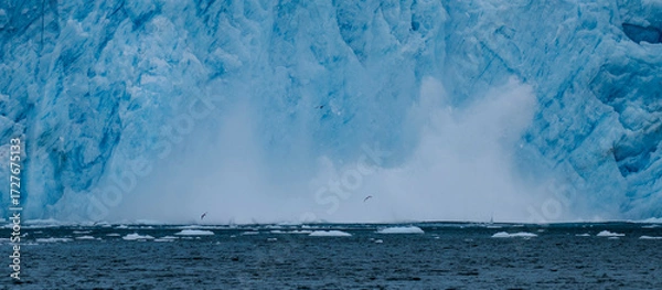 Fototapeta Aialik Glacier face calving ice bergs into the bay with seabirds flying in front of the mountainous spray of the splash provides perspective on its size