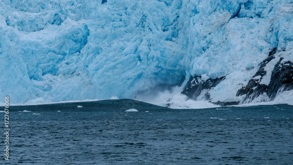 Fototapeta Calving action at Aialak Glacier causes a massive sea swell crashing into rocks