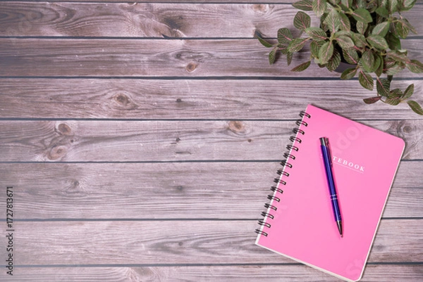 Fototapeta Pink spiral notebook on wooden table. Top view,Minimal workspace with notebook