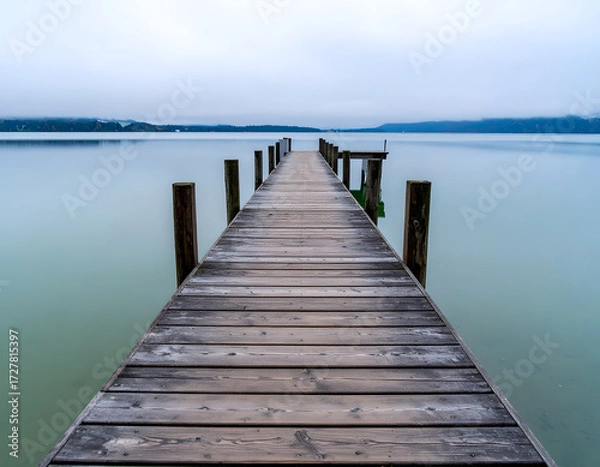 Fototapeta Tranquil Wooden Dock Extending into Calm Water Under Overcast Sky