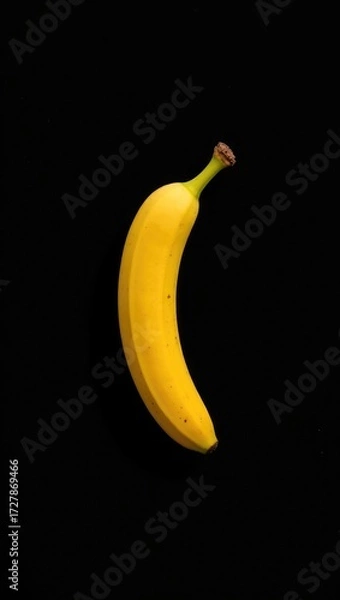 Fototapeta A single ripe yellow banana with a green stem isolated on a solid black background.
