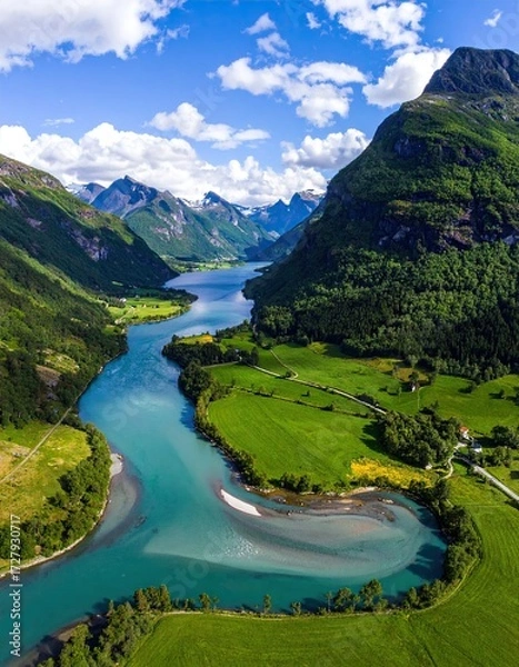 Obraz Aerial view of a turquoise river meandering through a lush green valley, nestled between majestic mountains under a vibrant blue sky
