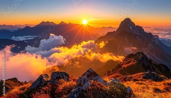 Obraz Vibrant sunset illuminates a mountainous landscape, casting golden hues on clouds and peaks; autumnal vegetation in the foreground