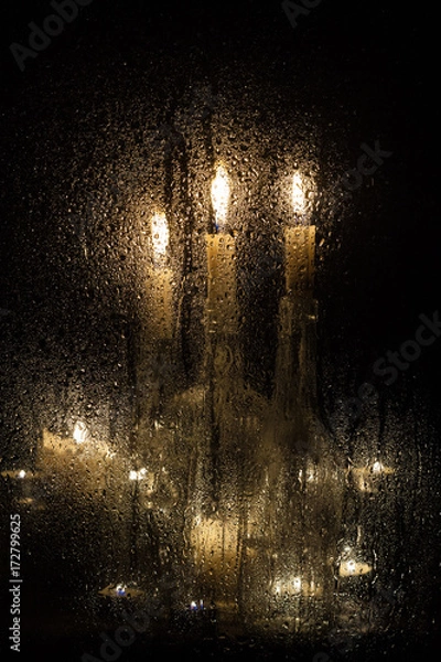 Obraz Candles and bottles behind a wet glass on a dark background.
