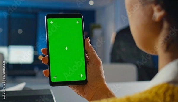 Fototapeta Close up view of a person holding a smartphone with a green screen, handheld cinematic shot with bokeh background, showcasing modern technology, digital interaction, and futuristic mobile device usage