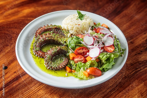 Fototapeta A modern and sophisticated seafood recipe. Grilled octopus served with spices, spicy lemon sauce, and aromatic herbs, accompanied by salad and rice on a white plate.