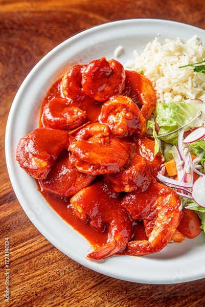 Fototapeta A plate of camarones a la diabla, spicy shrimp cooked in a rich red sauce, served with white rice and a side salad.