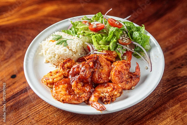 Fototapeta A plate of camarones a la diabla, spicy shrimp cooked in a rich red sauce, served with white rice and a side salad.