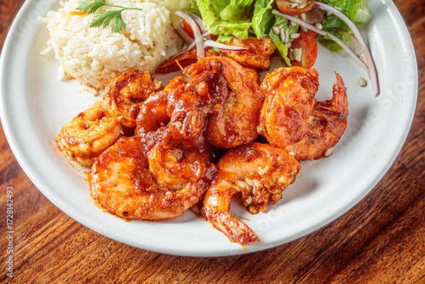 Fototapeta A plate of camarones a la diabla, spicy shrimp cooked in a rich red sauce, served with white rice and a side salad.