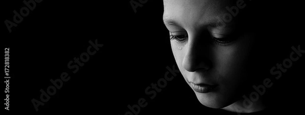Fototapeta The sad boy with tears in their eyes on a black background