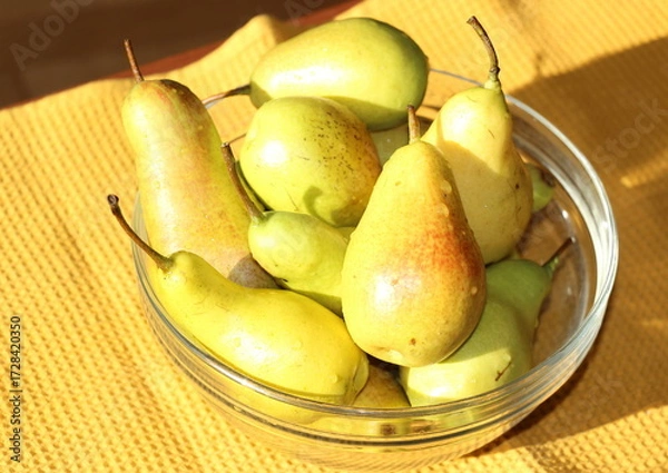 Fototapeta Ripe yellow-green pears in a transparent glass bowl on the table.