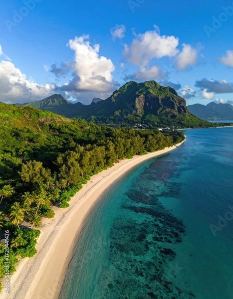 Fototapeta Aerial view of a pristine, crescent-shaped beach curving along turquoise water, backed by lush greenery and dramatic mountains under a vibrant blue sky
