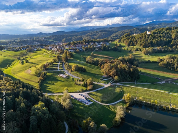 Fototapeta Aerial view of Gradišče near Lukovica, Slovenia, with a scenic church, lush fields, forest, and rolling hills under a tranquil sunset sky