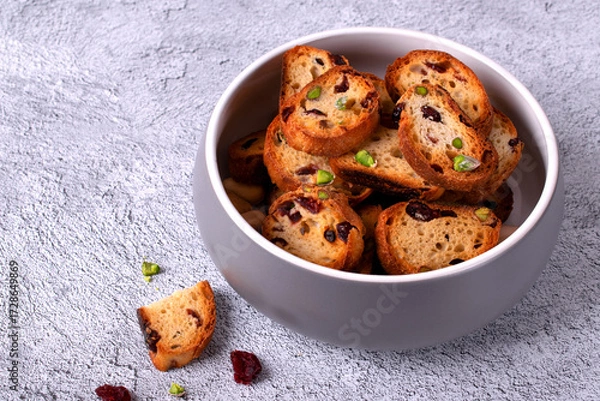 Fototapeta Rusks with dried cranberries and pistachios in ceramic bowl on light grey table