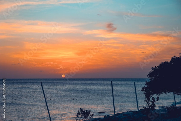 Obraz Floating in the waves at sunset, sun just above horizon, going down, orange sky, tranquil sea. Peaceful moment, vacations, summer mood. Dominican Republic. Horizontal video.