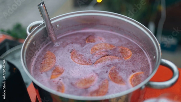 Fototapeta A close-up of hot mulled wine being prepared in a large metal pot. The brewing process of this traditional winter drink. Image used to illustrate recipes, Christmas traditions, and winter treats.