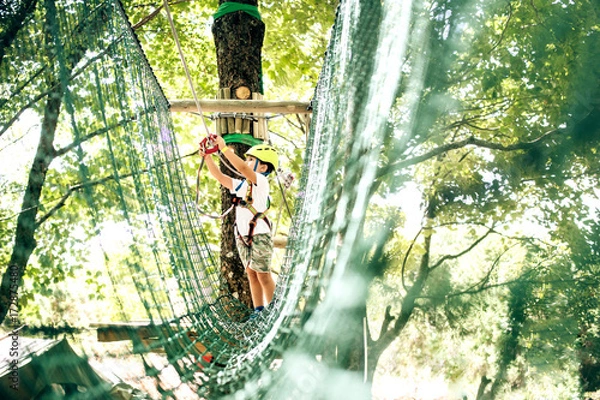 Obraz Happy Little Boy przechodzący trasę kablową wysoko wśród drzew, wspinaczka i gra, sport ekstremalny w Adventure Park