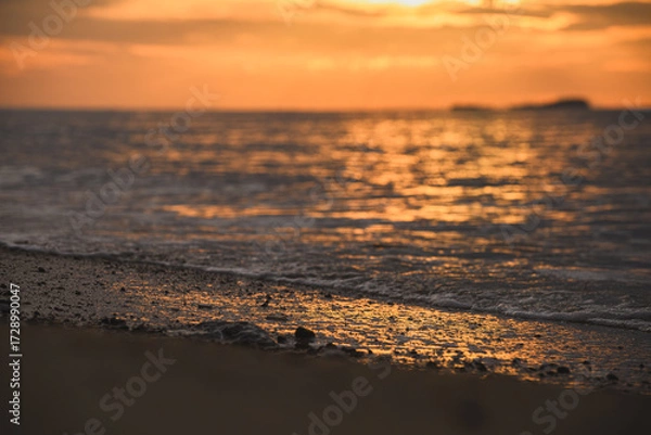 Fototapeta Golden morning light reflecting on ripples along sandy beach.