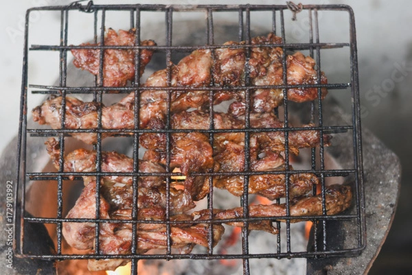 Fototapeta close-up shot of marinated meat grilling on a metal wire rack over an open flame or charcoal.