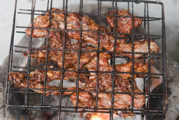 Fototapeta close-up shot of marinated meat grilling on a metal wire rack over an open flame or charcoal.