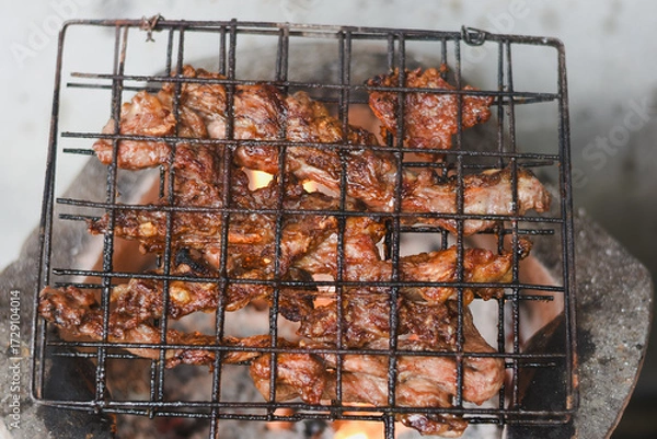 Fototapeta close-up shot of marinated meat grilling on a metal wire rack over an open flame or charcoal.