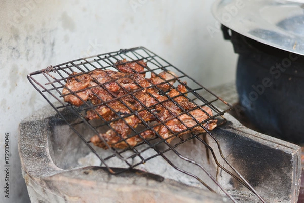 Fototapeta close-up shot of marinated meat grilling on a metal wire rack over an open flame or charcoal.