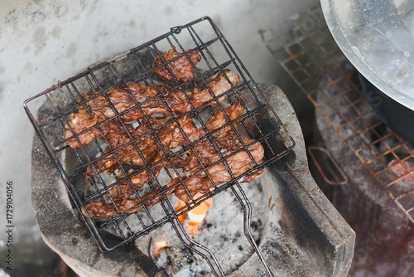 Fototapeta close-up shot of marinated meat grilling on a metal wire rack over an open flame or charcoal.