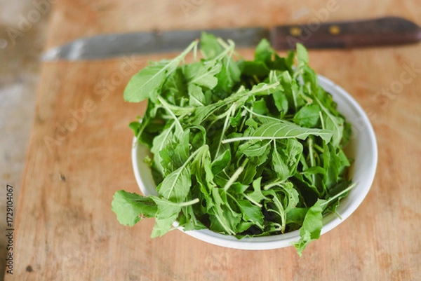 Fototapeta overhead shot focusing on a white bowl filled with fresh, bright green leaves placed on a light wooden surface.