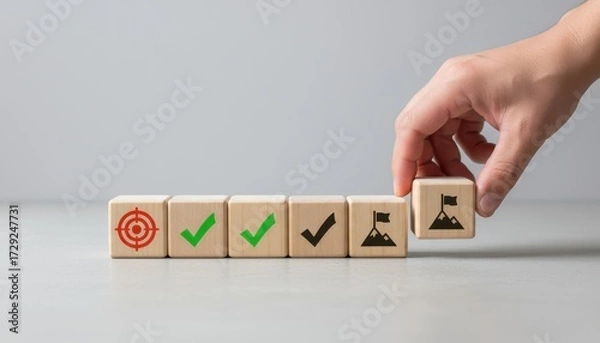 Fototapeta Goal Achieved: Hand places a cube block of wood with a flag icon, perfectly aligned with others, symbolizing the attainment of business goal, with minimalist design.
