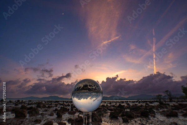 Fototapeta  A mesmerizing sunset over a rocky shoreline captured through a glass crystal ball, creating a surreal inverted reflection of the seascape beneath vibrant, colorful skies.