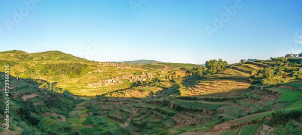 Obraz Afternoon sun shines to typical Madagascar landscape in region near Alakamisy Ambohimaha, small hills with terrace fields, clay houses village near