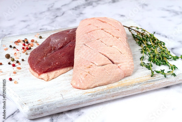 Obraz Fresh raw duck breasts, spread on a wooden cutting board, with herbs and spices, on a white marble surface
