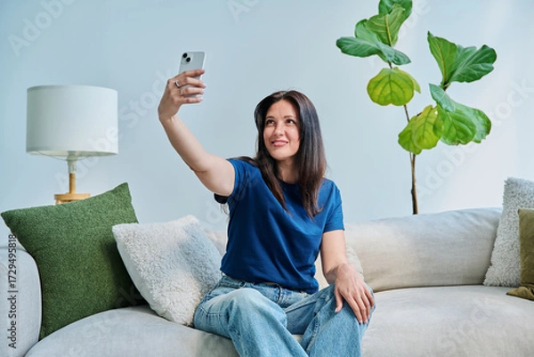 Fototapeta Happy beautiful woman taking selfie portrait on smartphone, at home