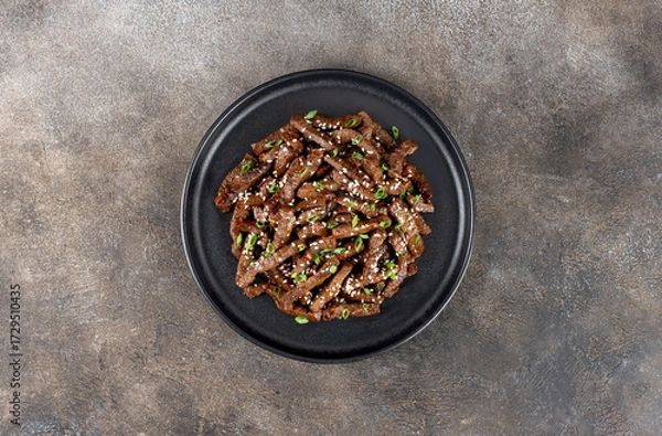 Fototapeta Stir-fry beef marinated with teriyaki sauce, green onions, and sesame seeds on a dark background. Top view