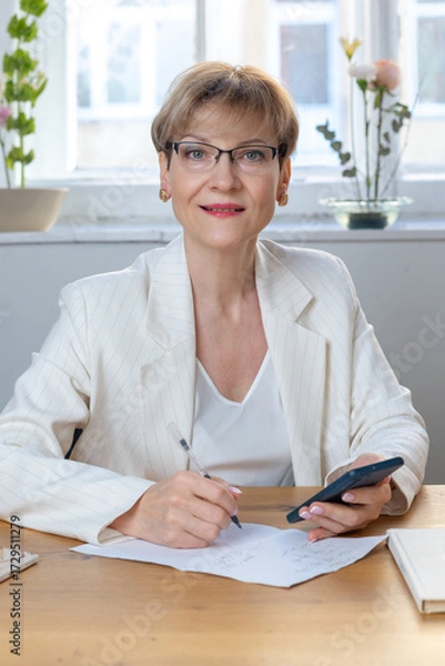 Obraz Portrait of business woman. Confident mature woman using mobile phone and typing. Vertical photo. High quality photo