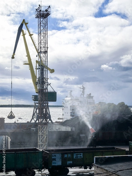 Fototapeta Harbor scene showing a large crane loading coal onto a shipin a bustling port, with industrial machinery and waterfront in the background, highlighting trade activities.