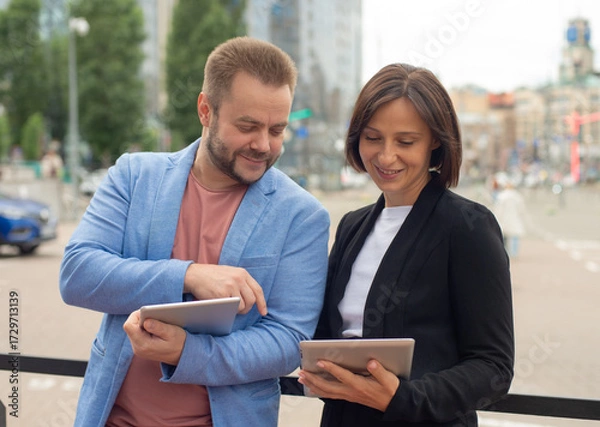Fototapeta Businesspeople using a tablet computer in the city. A businessman and businesswoman consult, plan, discuss, and use a tablet.