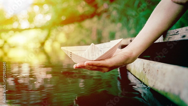 Obraz A boy from the palm of his hand lowers a paper boat into the water