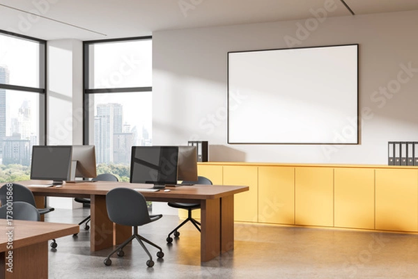Fototapeta Modern office interior with large blank poster frame on wall and computer desks near windows overlooking cityscape in daylight. 3D Rendering