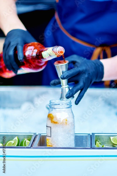 Fototapeta Bartender is pouring alcohol from a measuring glass into a glass over ice