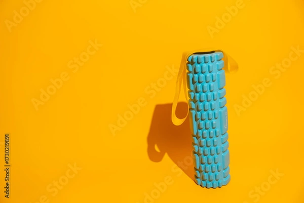 Fototapeta Standing foam roller with yellow resistance band on vivid yellow background strong shadow fitness recovery concept. High quality photo