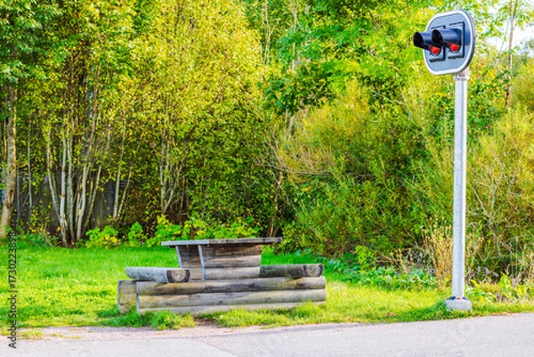 Fototapeta Wooden bench with table in park near traffic signal light surrounded by green trees and grass. Sweden.