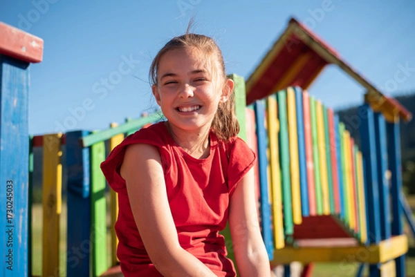 Fototapeta Smiling child girl playing on a colorful playground structure in a sunny park, enjoying a fun and active outdoor moment.