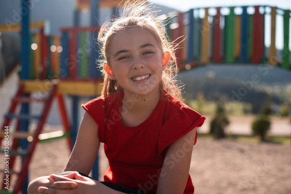 Fototapeta Smiling child girl playing on a colorful playground structure in a sunny park, enjoying a fun and active outdoor moment.