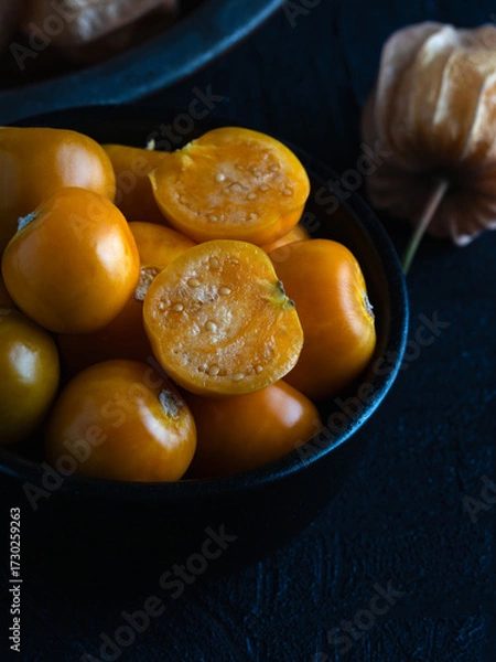 Obraz Close-up of fresh golden berries, also known as physalis or ground cherries, in a black bowl on a dark textured background.