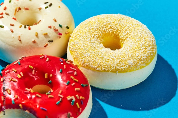 Fototapeta Overhead view of various donuts with confetti arranged on colored background