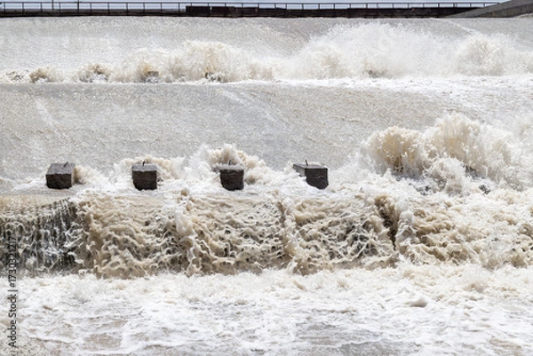 Fototapeta Turbulent water flowing over concrete blocks at dam