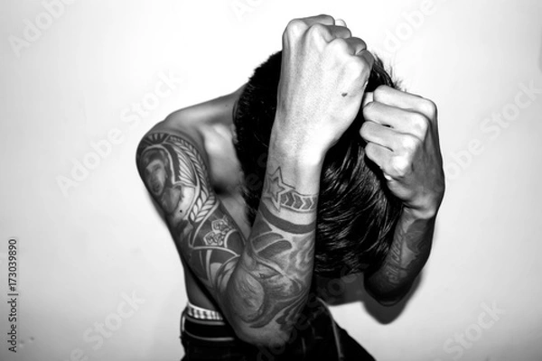 Fototapeta A young man without a shirt, with his hands full of tattoos. High Key Photo with black and white filter color. 