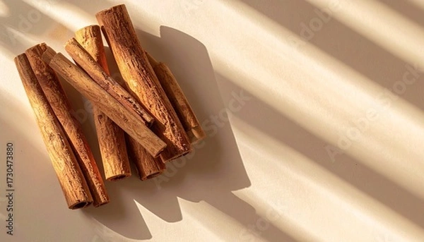 Fototapeta Pile of cinnamon sticks casting warm shadows on a light surface.
