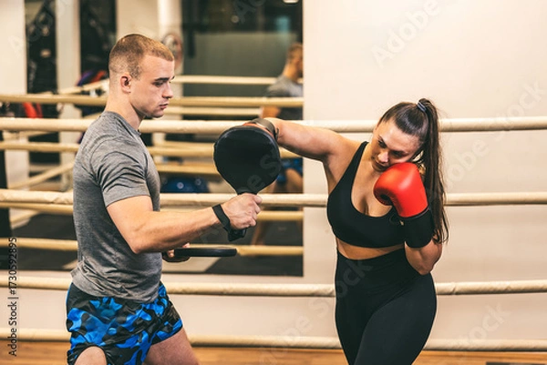 Fototapeta Training session in boxing gym with a male coach and female athlete working on technique